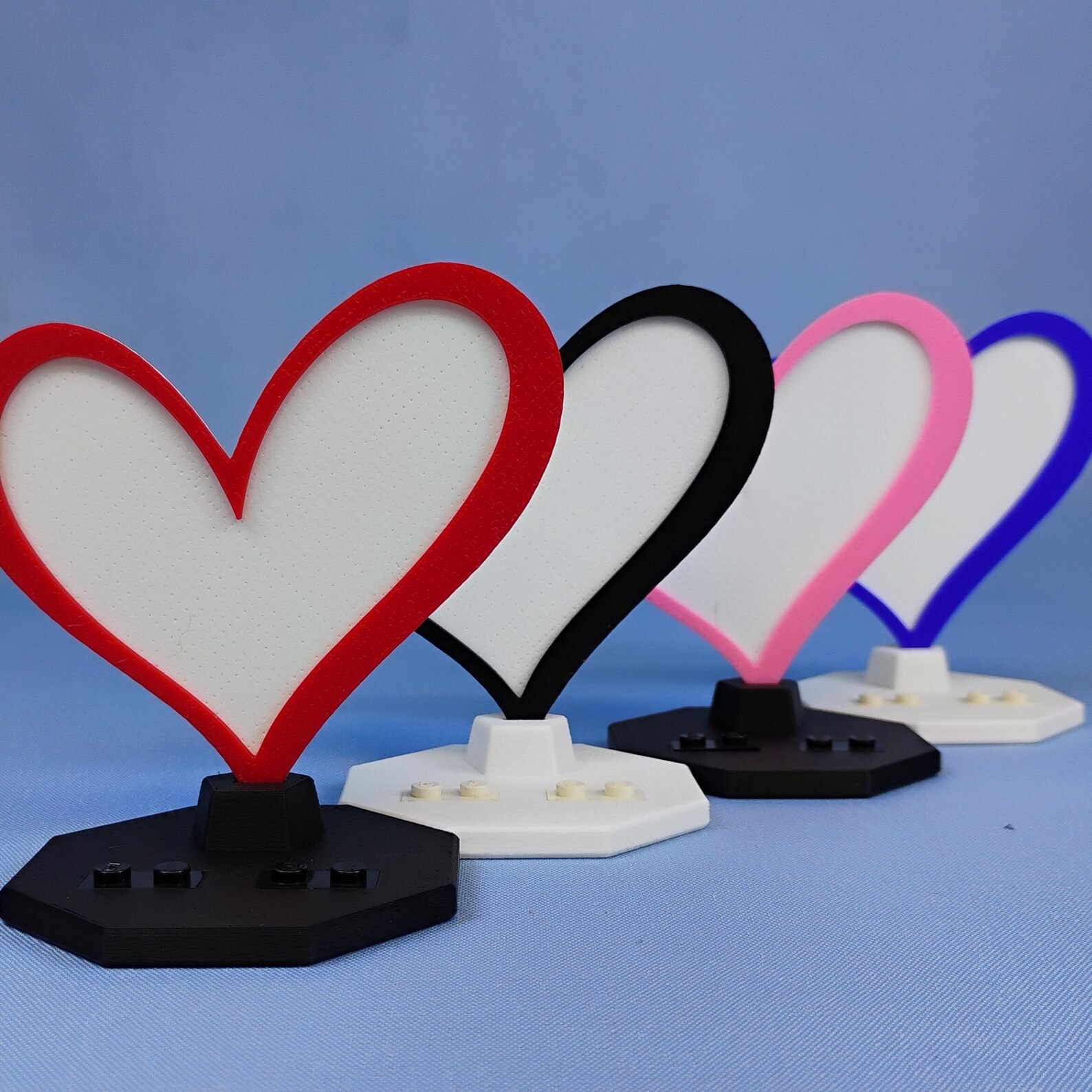 Multiple Heart Displays for LEGO® minifigures shown together to demonstrate available heart accent colors with black and white base options for customizable desk or shelf decor.